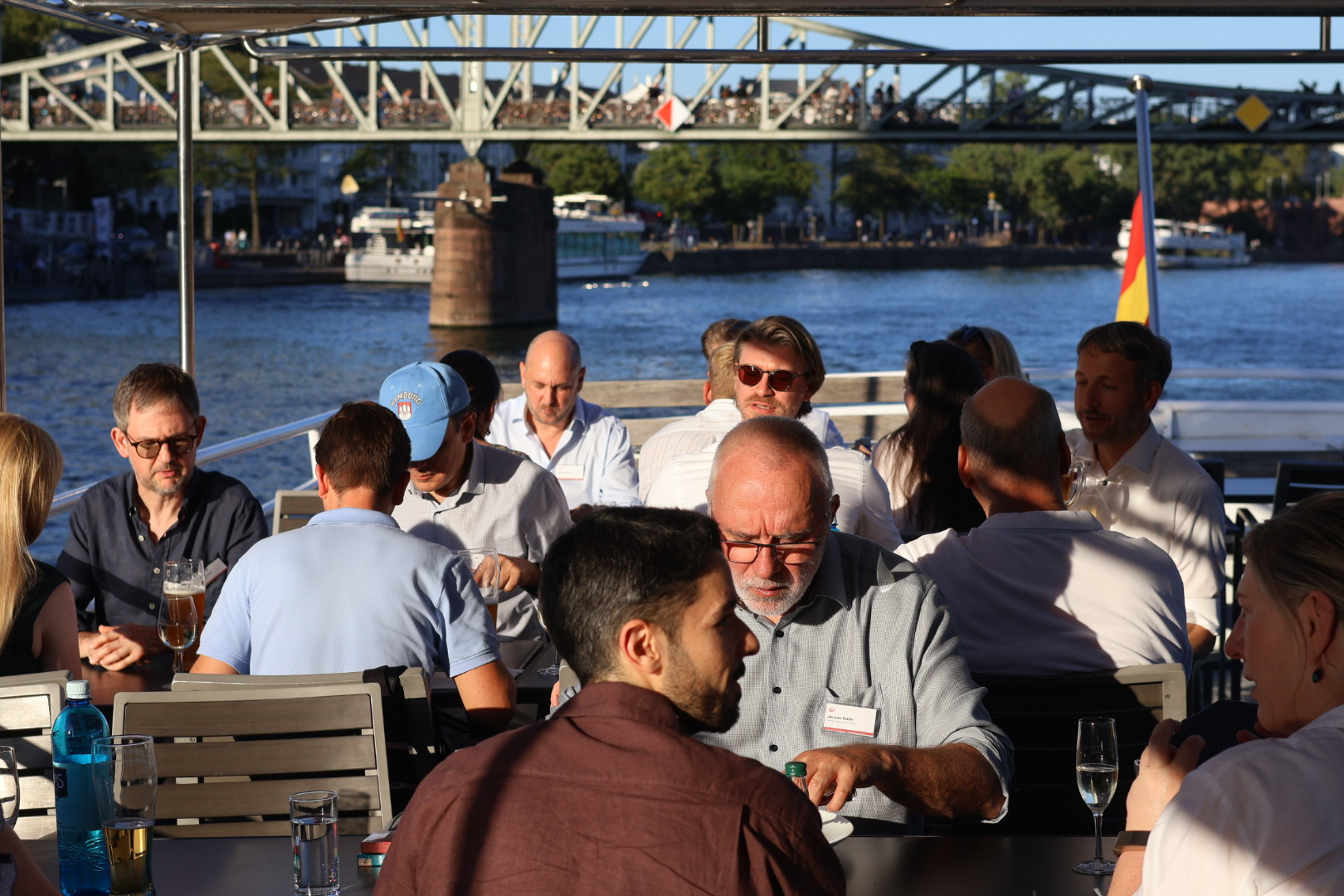 Gäste des RA-MICRO KI-Abends sitzen auf dem Schiffsdeck zusammen und führen Gespräche vor einer Mainbrücke.