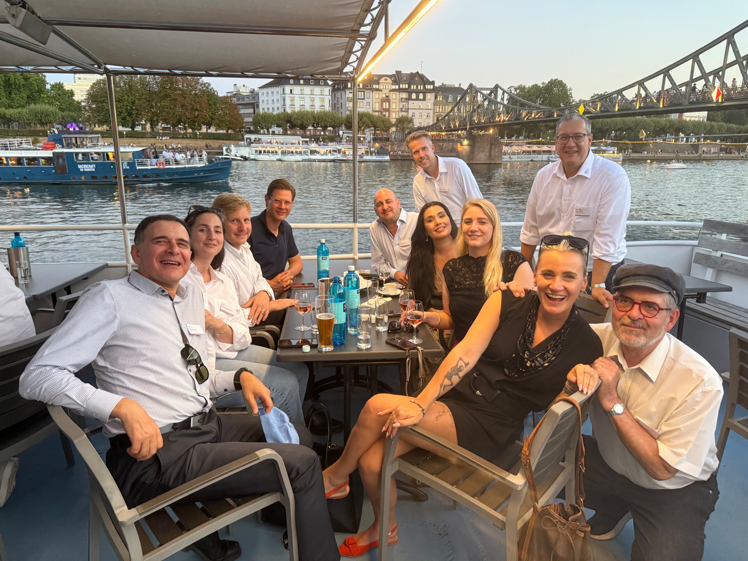 Teilnehmende des RA-MICRO KI-Abends posieren gemeinsam an einem Tisch auf dem Schiff vor dem Eisernen Steg.