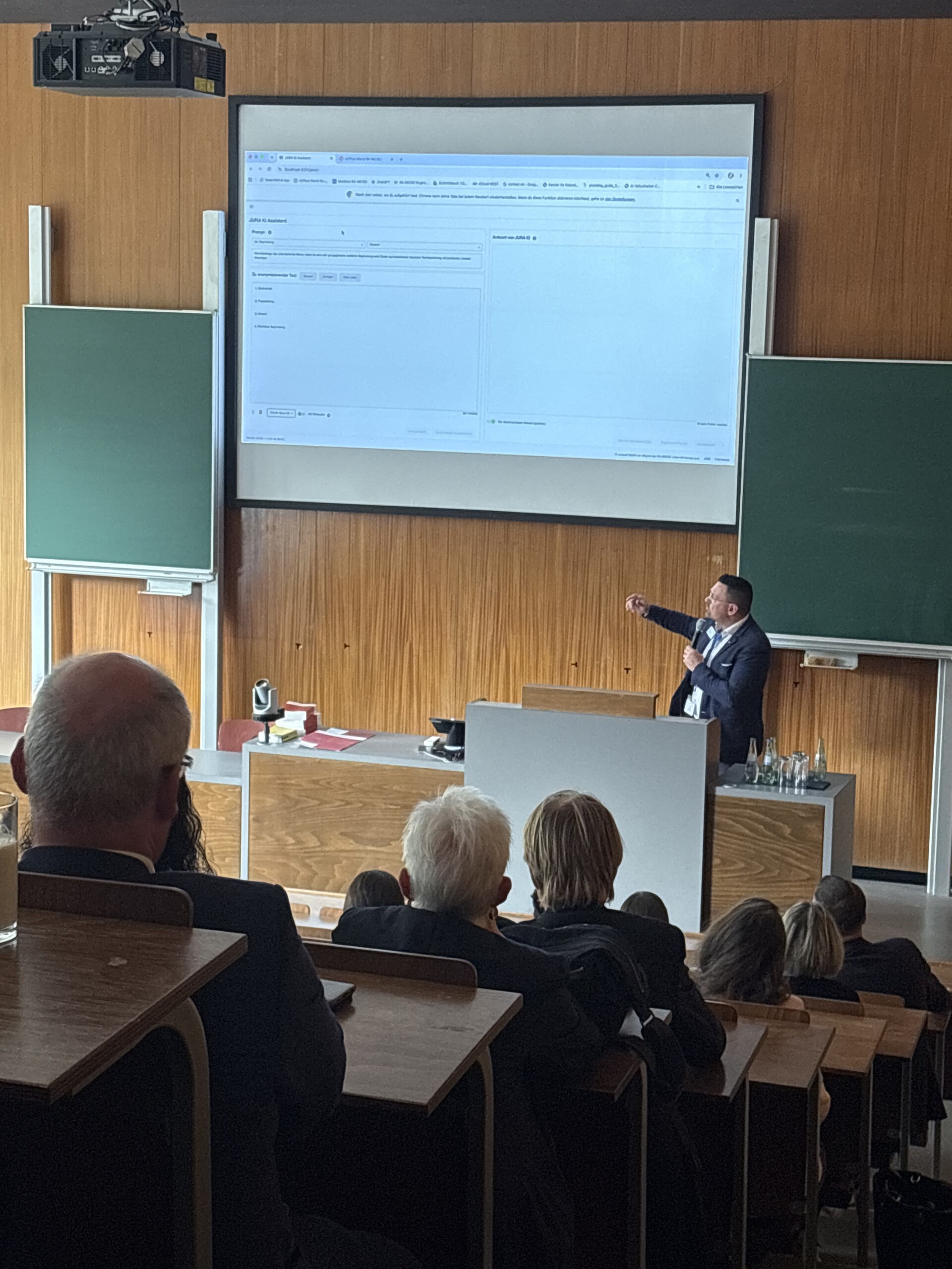 René Kurtkowiak hält beim EDV-Gerichtstag 2026 vor Publikum einen Vortrag und präsentiert eine KI-Anwendung auf einer großen Leinwand.